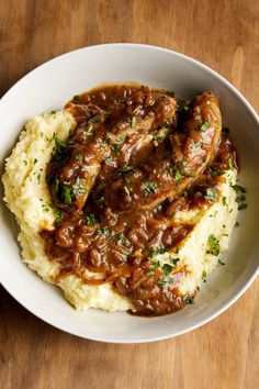 mashed potatoes topped with meat and gravy in a white bowl on top of a wooden table