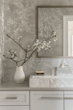 a white vase filled with flowers sitting on top of a bathroom counter next to a mirror