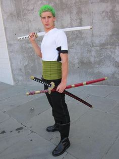 a man with green hair is holding two swords in his hands and posing for the camera