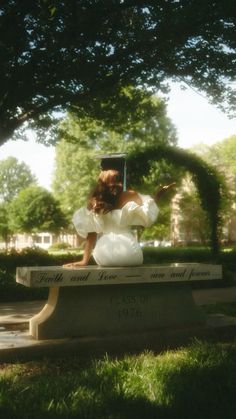 a woman sitting on top of a bench under a tree in a park with grass