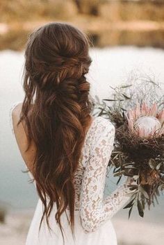 a woman with long hair holding a bouquet in her hand and looking at the water