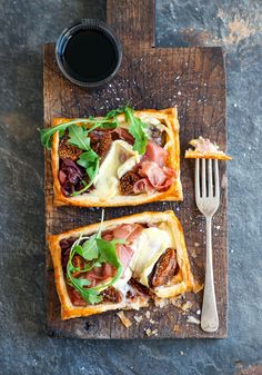 two pieces of bread with meat, cheese and greens on it next to a fork