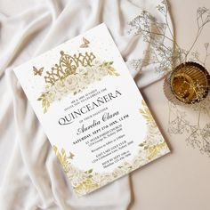 a white and gold wedding card with a tiara on it next to some flowers