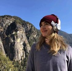 a woman wearing headphones standing in front of mountains