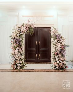 an entrance decorated with flowers and greenery in front of a wooden door at a wedding