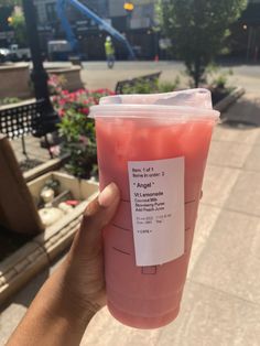 a person holding up a plastic cup with pink liquid in it's sleeve and label