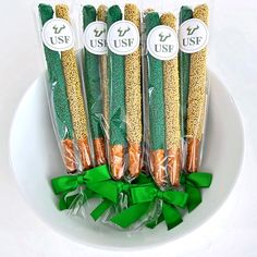 four green and gold colored straws in plastic wrappers on a white plate with ribbon