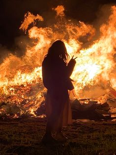 a woman standing in front of a fire with lots of flames coming out of it