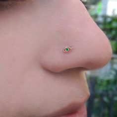 a woman's nose with a small green eye piercing on the tip of her nose