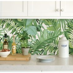 a kitchen counter with plates, bowls and bottles on it in front of a tropical wallpaper