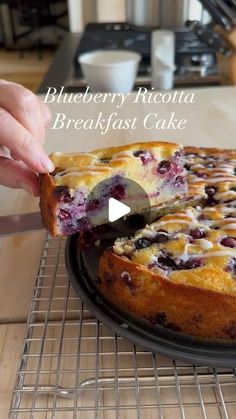 blueberry ricotta breakfast cake on a cooling rack with a slice being taken out