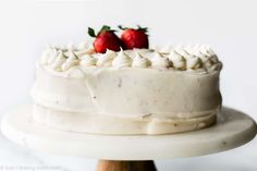 a cake with white frosting and two strawberries on top is sitting on a stand