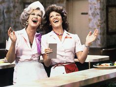 two women are laughing and holding papers in their hands