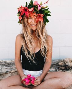 a woman sitting on the ground with flowers in her hair and wearing a flower crown