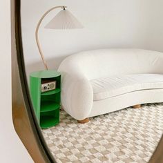 a white couch sitting on top of a rug next to a green book shelf and lamp