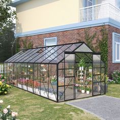 a small greenhouse with plants in it on the side of a brick building next to some flowers