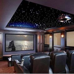 a home theater with black leather seats and stars painted on the ceiling over the screen