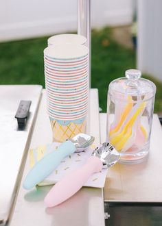 a table topped with lots of different colored utensils next to a stack of cups