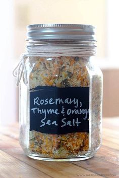 a jar filled with sea salt sitting on top of a wooden table next to a sign that says rosemary, thyme and orange sea salt