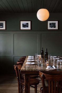 a dining room table set with place settings and wine bottles on the wall behind it