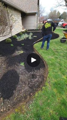 two men are working in the yard with black mulch