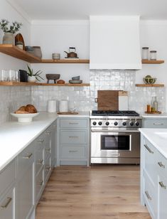 a kitchen with gray cabinets and white counter tops is pictured in this image, there are wooden shelves above the stove