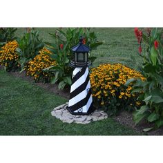 a black and white striped light house in the middle of some flowers with yellow flowers around it