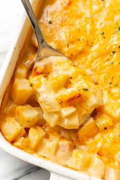 a spoon in a casserole dish with potatoes and cheese on the side, ready to be eaten