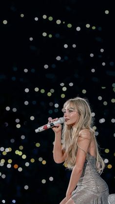 a woman in a silver dress is holding a microphone and singing into the air with confetti floating around her