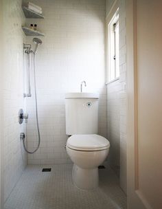 a white toilet sitting inside of a bathroom next to a shower head mounted on a wall