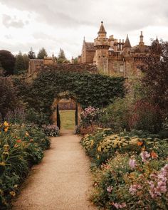 an old castle with lots of flowers in the foreground and a path leading to it