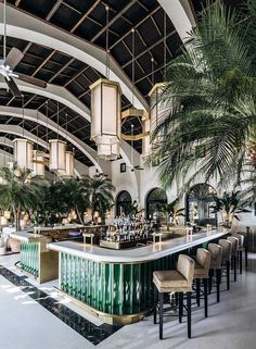 an indoor bar with lots of chairs and palm trees in the center, surrounded by tall ceilings