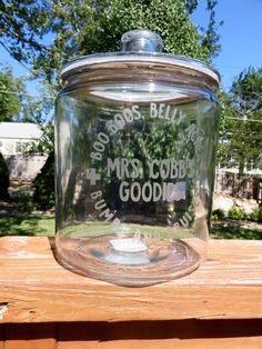 a glass jar sitting on top of a wooden table next to some grass and trees