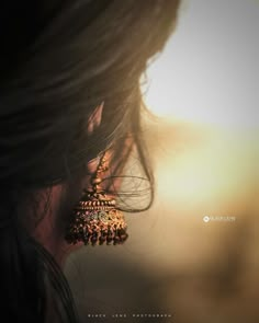 the back of a woman's head with earrings hanging from her ear and hair blowing in the wind