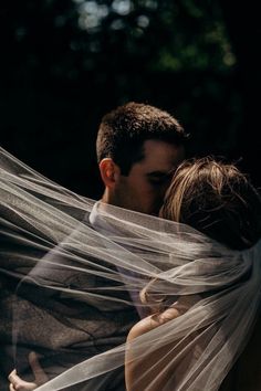 a man and woman kissing under a veil in the dark with trees in the background