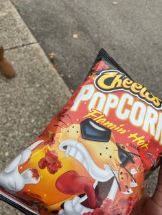 a hand holding a bag of cheetos popcorn on the sidewalk next to a person