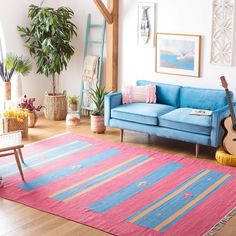 a living room with a blue couch, pink rug and potted plant in the corner