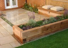 a wooden planter filled with lots of plants next to a brick wall and green grass