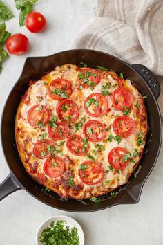 a pizza in a skillet with tomatoes and parsley on the table next to it