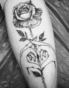 a black and white photo of a person holding a rose tattoo on their left leg