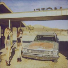 two women standing in front of an old car