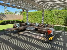 an outdoor living area with couches and chairs under a pergolated roof in the sun