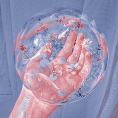 a person's hand holding a clear bubble filled with water and small red butterflies