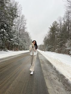 a woman standing on the side of a road in the middle of snow covered trees