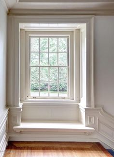 an empty window seat in the corner of a room with wood floors and white walls