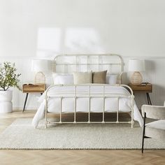 a white bed sitting on top of a wooden floor next to two chairs and a table