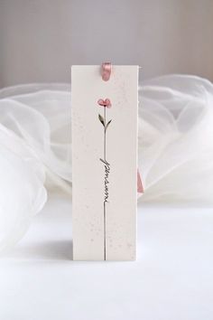 a card with a pink flower on it sitting on a white tablecloth covered bed