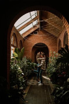 two people standing in the middle of a brick building surrounded by plants and greenery