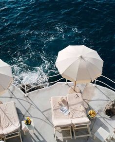 chairs and umbrellas on the deck of a boat in the ocean with water behind them