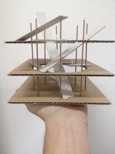 a hand is holding up a model of a building with metal bars sticking out of it's sides